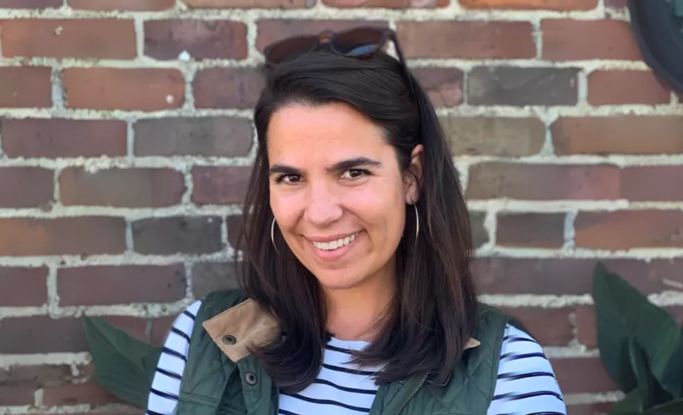 Smiling woman with dark brown hair and sunglasses pushed back on her head wearing a striped shirt