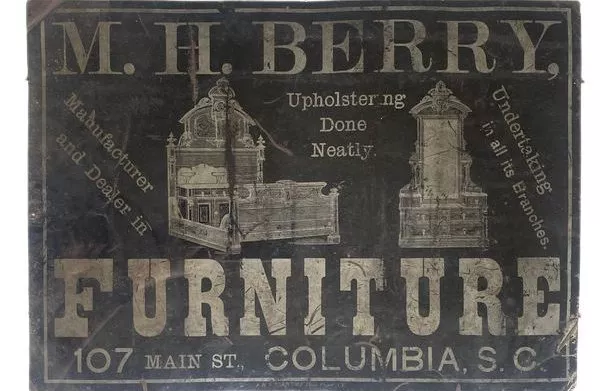 M.H. Berry Furniture sign. Dark background with lighter grey lettering. 